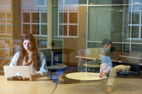 A student viewed through a glass window using a laptop computer