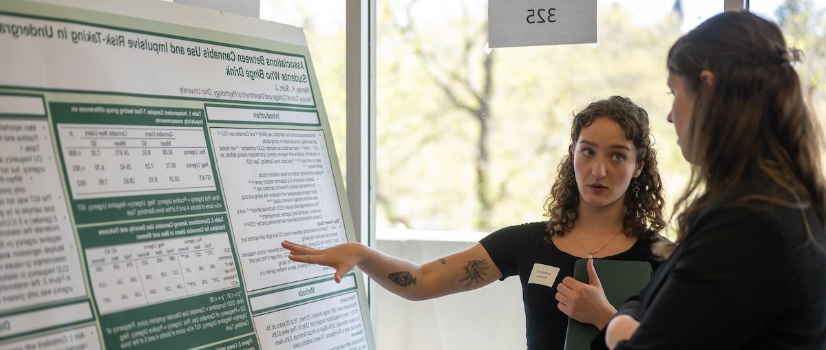 A photo of a student talking about their research with an onlooker.