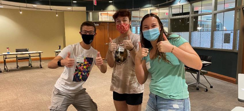 Three students give a thumbs up to the camera